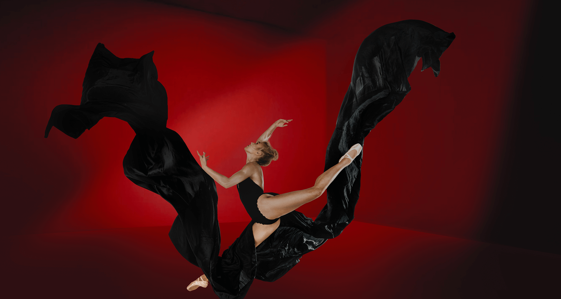 Dancer in flowing black fabric against a red studio backdrop